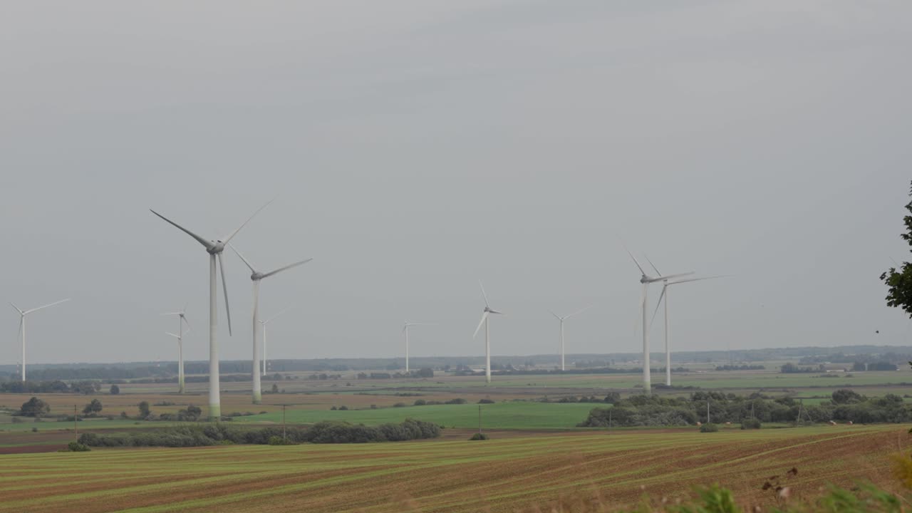 Wide-angle view of multiple wind turbines generating renewable energy across green and brown fields on an overcast day in the countryside