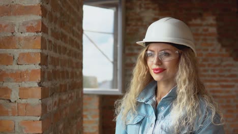 a young woman in a white work helmet and denim clothes and goggles stands at the construction site. builder, bricklayer, architect