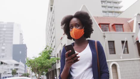 Mujer-Afroamericana-Con-Máscara-Facial-Usando-Un-Teléfono-Inteligente-En-La-Calle