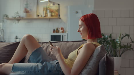 chica relajada chillando en el sofá en casa, navegando por la web en su teléfono inteligente