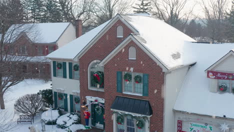 aerial of front exterior of house covered in snow, decorated for christmas