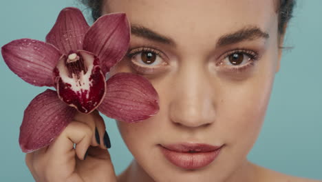 close-up-portrait-beautiful-woman-playfully-flirting-with-orchid-flower-looking-seductive-perfect-skin-complexion-enjoying-healthy-skincare-on-blue-background