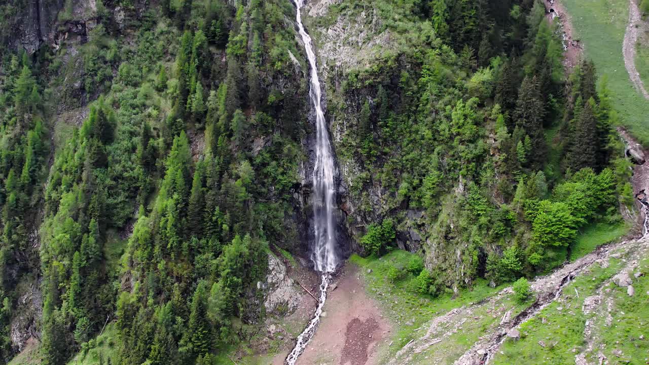Cascata pittoresca su un versante montano circondata da alberi, con zoom in.