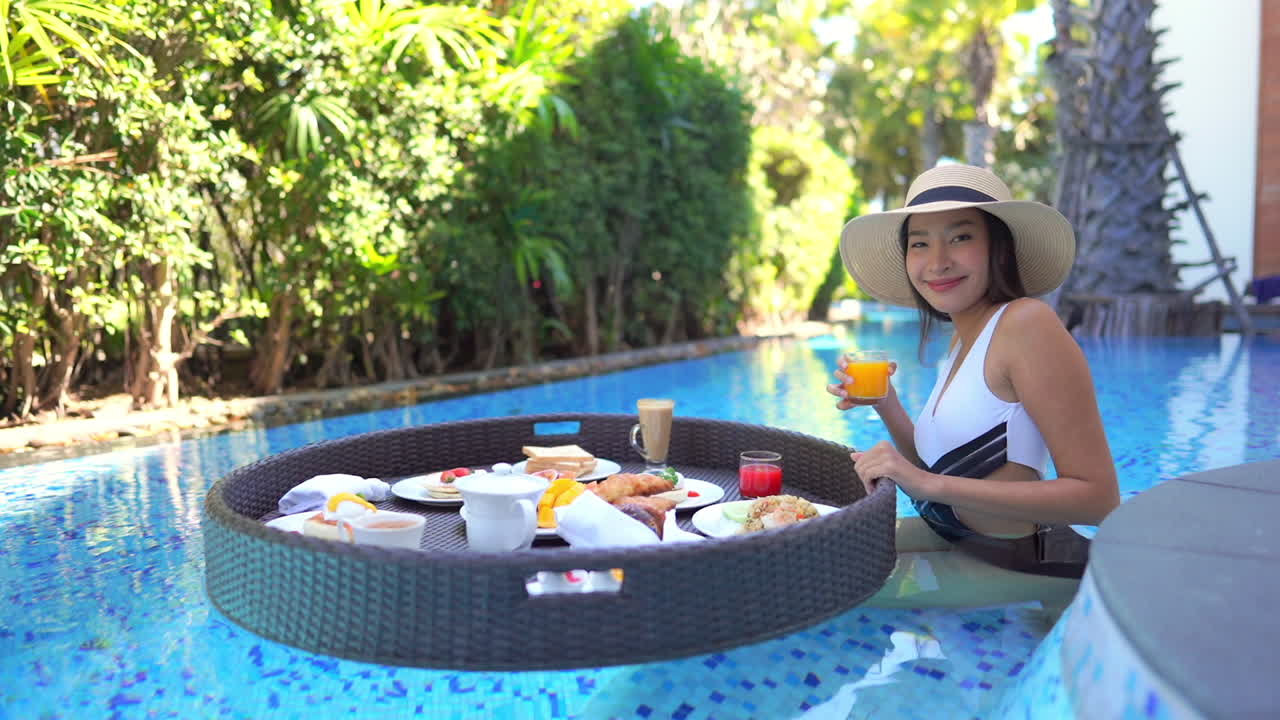 An Asian woman relaxing in a resort pool selects orange juice form the floating brunch buffet