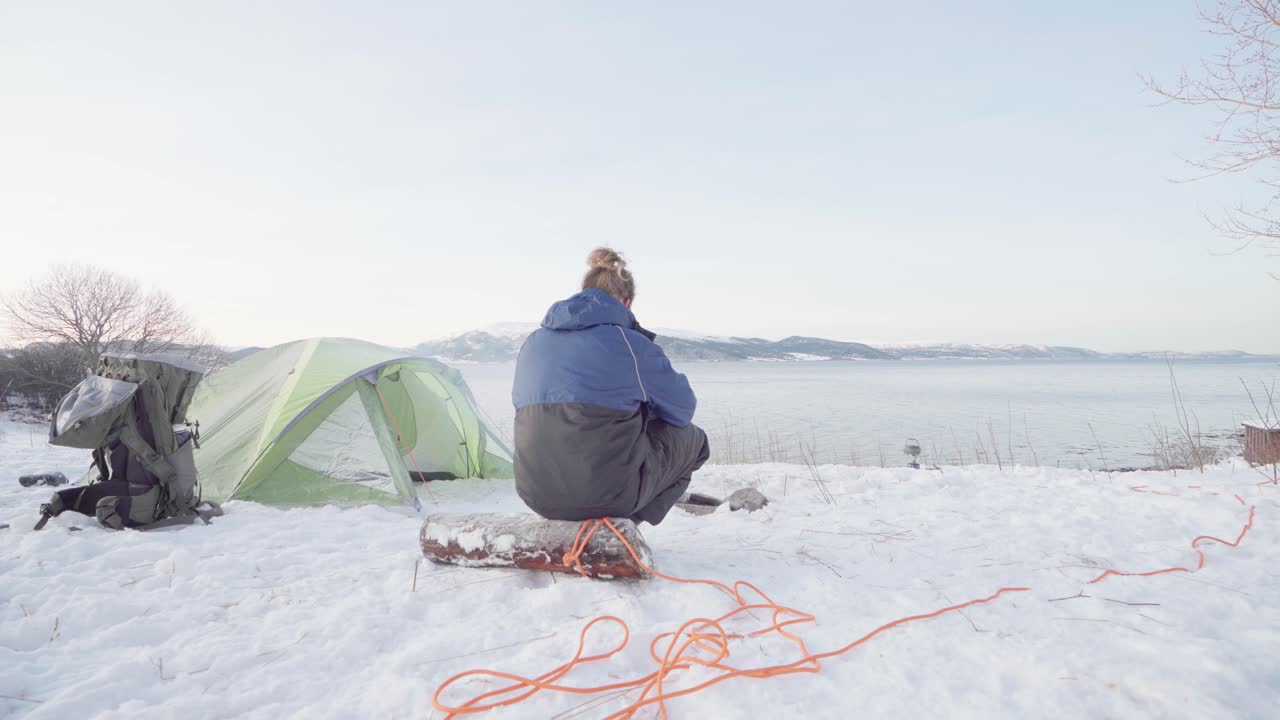 겨울에 텐트 밖에서 모닥불 옆에 있는 통나무에 앉아 있는 남자
