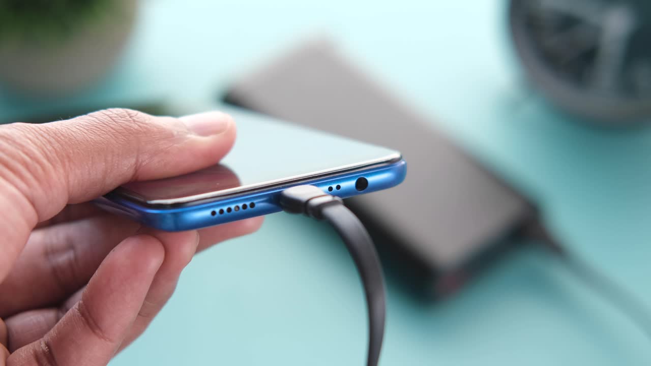 mano sosteniendo un teléfono inteligente azul que se está cargando.