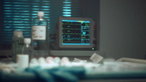 Hospital-heartbeat-monitor-screen.-Closeup-medical-instruments-glove-on-table.