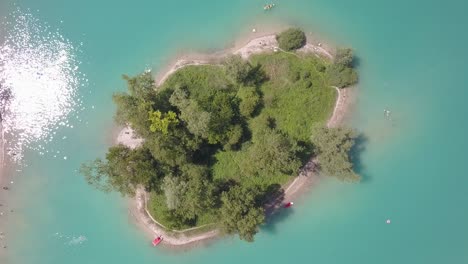 Antena-De-Arriba-Hacia-Abajo-De-Una-Pequeña-Isla-En-Medio-De-Un-Lago-Azul-En-Los-Alpes-En-Italia,-Lago-Di-Tenno-Cerca-De-Ville-Del-Monte,-Italia