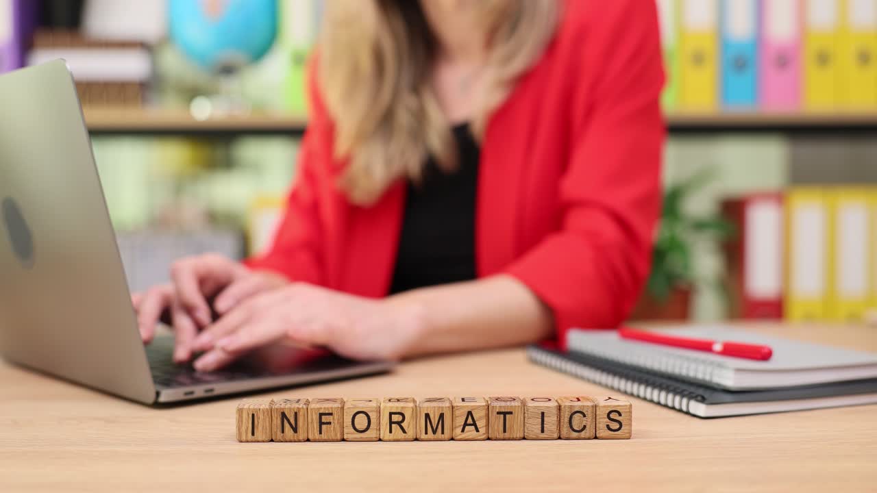 Woman working on laptop with "INFORMATICS" spelled out in wooden blocks