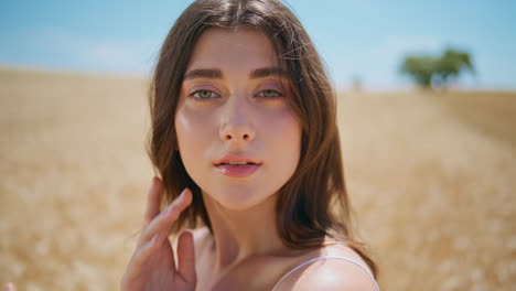 gentle brunette arranging hair in sunlight field summer portrait. woman posing
