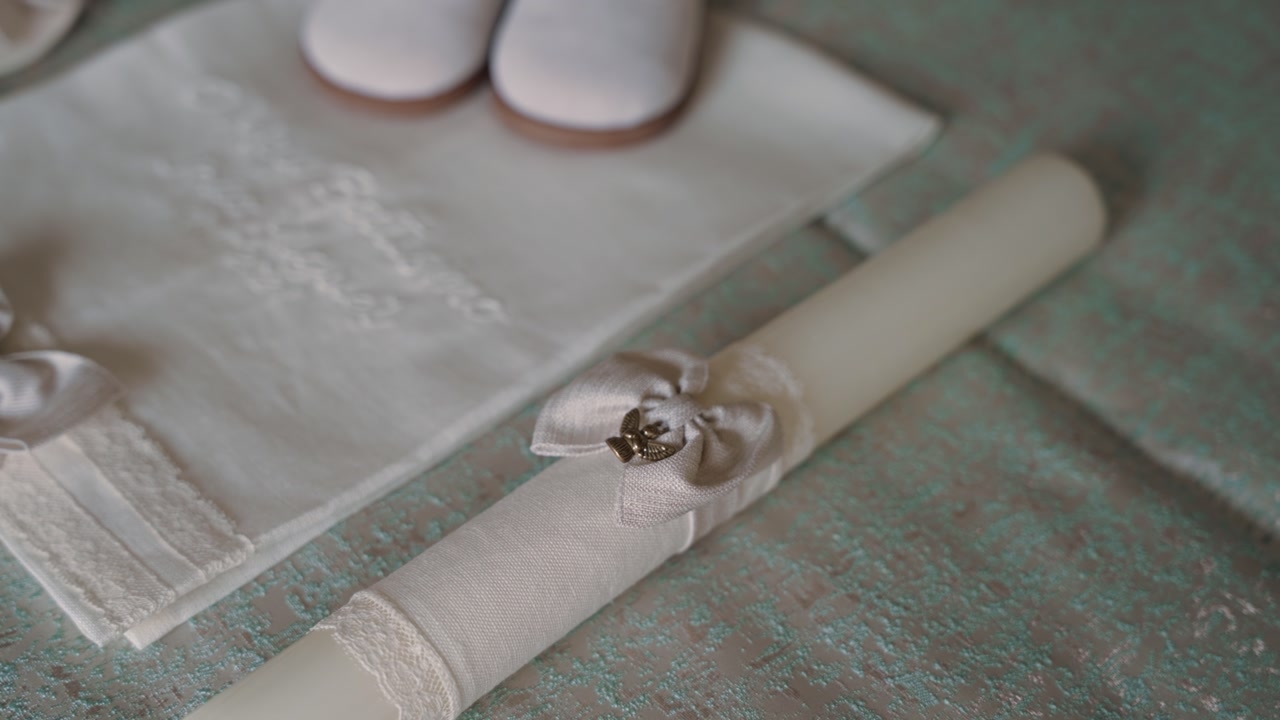 Close up of white baptism candle and embroidered cloth placed on a table before ritual