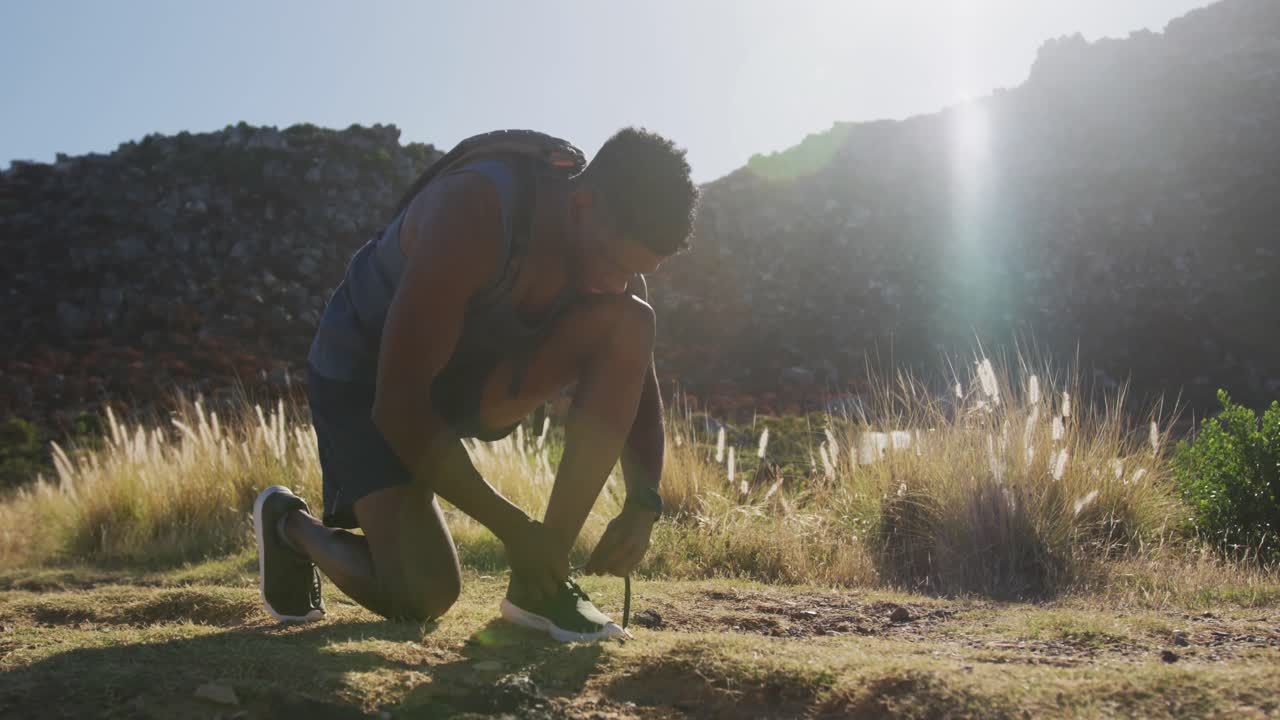 hombre afroamericano haciendo ejercicio al aire libre atando su zapato en el campo en una montaña