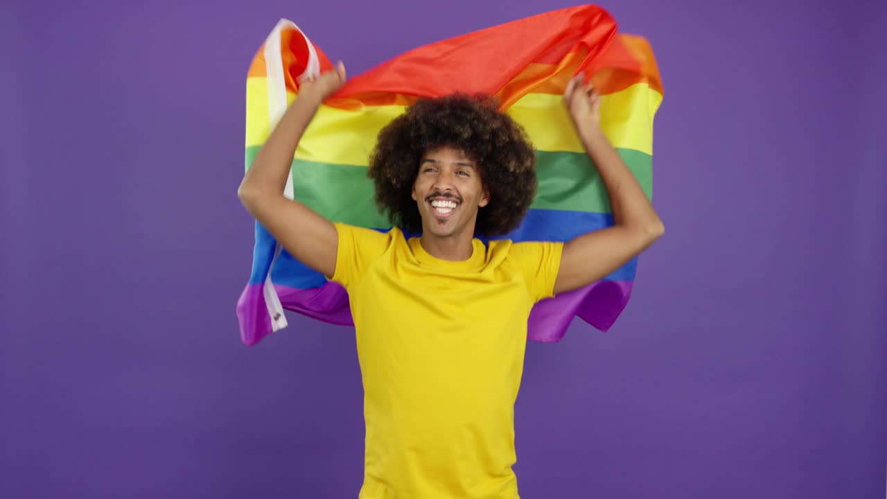 Person with afro holding a rainbow flag on a purple background