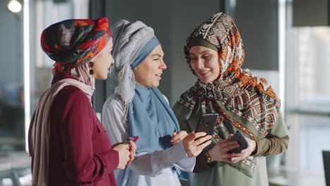 female colleagues in hijabs using smartphone and talking