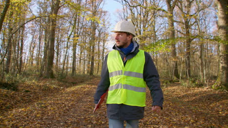 ingeniero masculino caminando solo hacia la cámara en el bosque mientras lleva un clipboard para inspeccionar árboles, de mano siguiendo