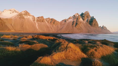 Golden-Vestrahorn-Mountain-Sunrise-Y-Stokksnes-Marea-Baja-Hierba-Marina-Que-Crece-En-La-Playa-De-Arena-Negra,-Vista-Aérea