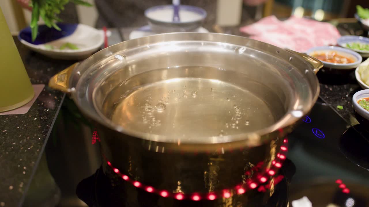 Hand places leafy greens into simmering hotpot broth, kitchen countertop, warm indoor lighting, close-up
