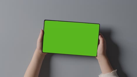 overhead shot of child holding green screen digital tablet horizontally watching or streaming content