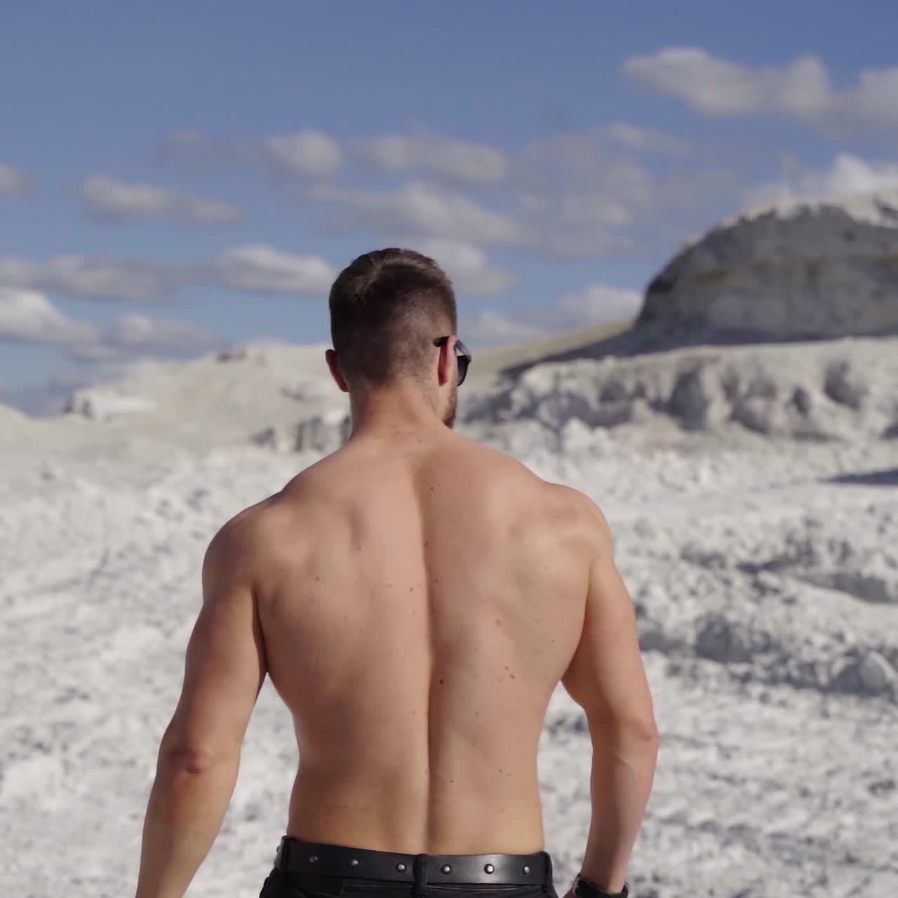 Athlete in bright sunny day on white canyon. Backside view of sporty man in nature. Shirtless bodybuilder walks in the mountains to the black car. Slow motion.