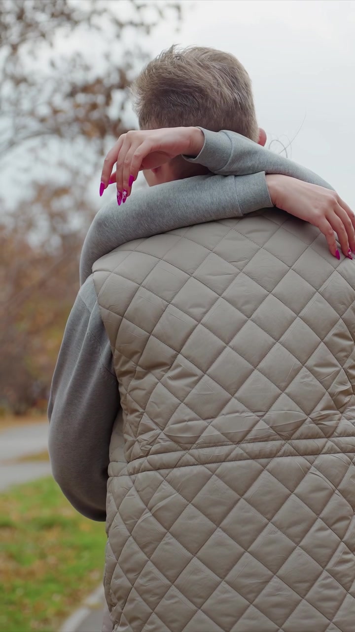 Kapitone yelekli bir erkek figürü, çevrili bir patikada ilerliyor. Pembe boyalı rakamlar, bej yelekli kişinin üst kısmına sürtünüyor. Ağaçlarla çevrili patikası olan park benzeri bir ortamda düşmüş yapraklar görülüyor.