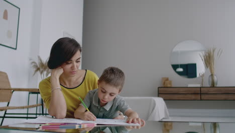 beautiful young mother in a warm sweater lying on the floor with my son drawing with markers on paper portraying his family. the child learns to draw