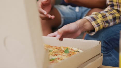 Diverse-male-teenage-friends-eating-pizza-and-sitting-on-couch,-slow-motion