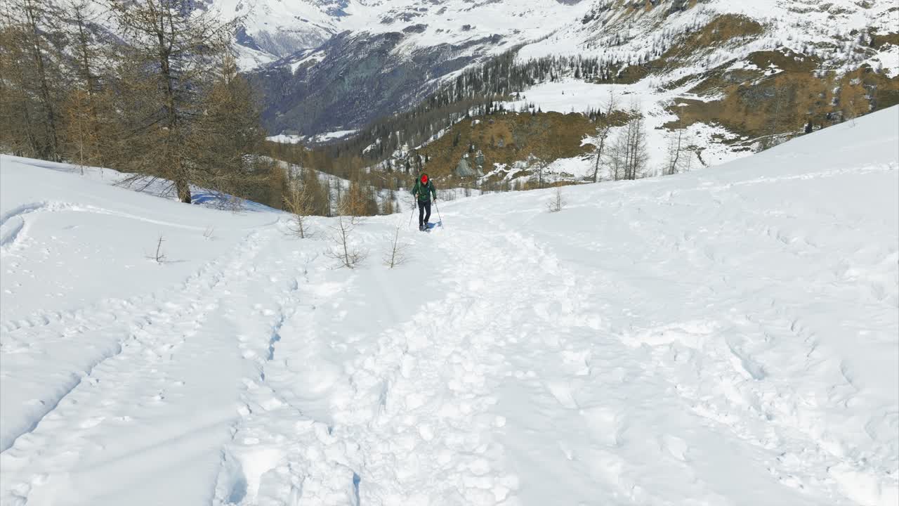 Escursionista che ciaspola in salita su un sentiero di montagna innevato, avventura invernale in paesaggio alpino. Ideale per sport all'aria aperta, viaggi, fitness, contenuti di esplorazione. Ripresa da dietro.