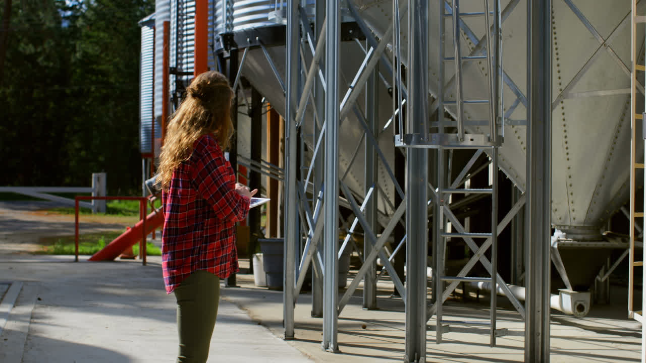 vista lateral de una trabajadora caucásica mirando tanques de almacenamiento trabajando en una tableta digital 4k
