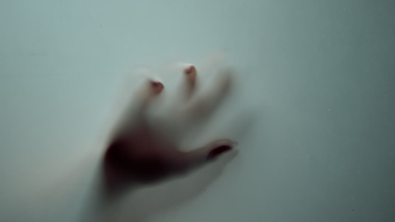 Macro di mano che saluta dietro un vetro smerigliato. Dita femminili che scorrono sulla superficie di vetro.