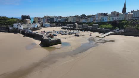 Tenby-Seaside-town-harbour-with-tide-out-in-Pembrokeshire,-Wales,-low-PoV-Aerial-4K-footage