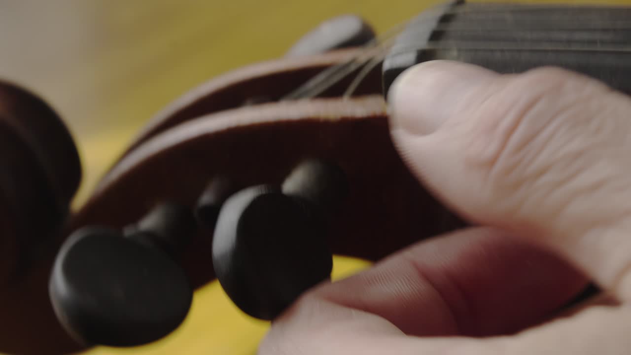 Musician turns pegs to tune nylon strings on antique violin Close-Up