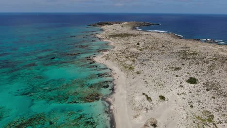 rocky shore of elafonissi beach peninsula in crete greece with clear azure waters, aerial dolly in shot