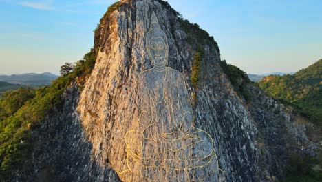 4k-Aerial-Pan-back-above-carved-Buddha-Image-made-from-Gold-on-a-cliff-at-Khao-Chee-Chan,-Pattaya,-Thailand