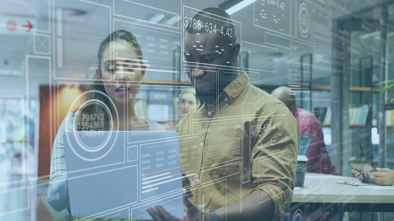 Two coworkers standing, reviewing laptop when overlay updating, pointing and clarifying data