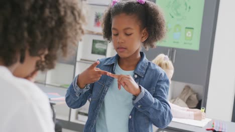 video of diverse schoolboy and schoolgirl practicing sign language in classroom