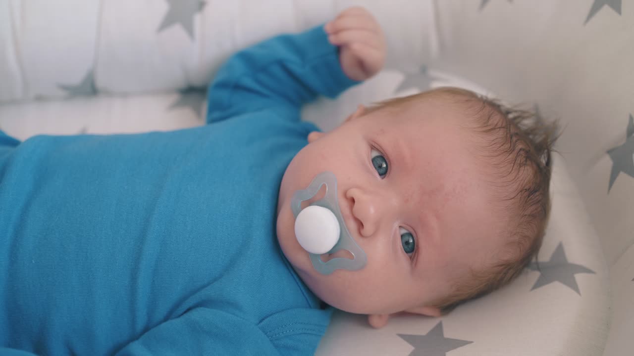 ledset litet spädbarn suger napp i kokong i vagga