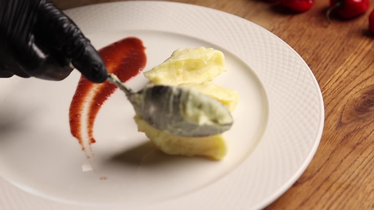 Chef Plating Mashed Potato Dumplings with Red Sauce on a White Plate