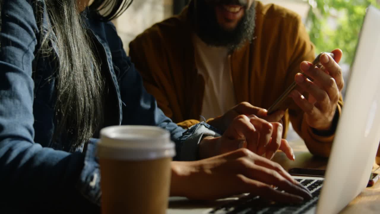 Giovane coppia di etnia mista che discute usando il cellulare al tavolo al bar 4K