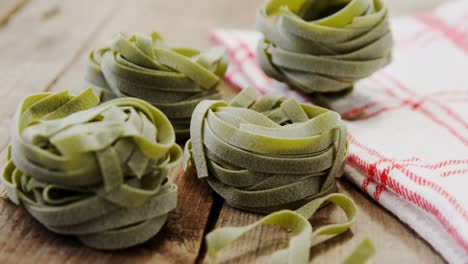 Roll-of-green-tagliatelle-pasta-with-white-and-red-napkin-on-wooden-table-background