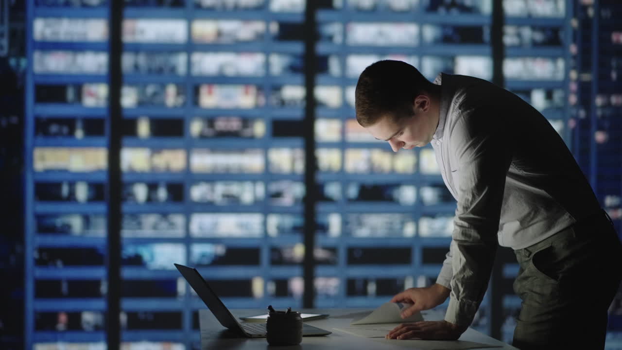 Deal with the report until late at night in the office standing at the table against the background of the night city