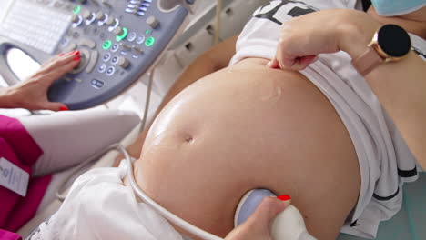 pregnant woman doing ultrasound in modern clinic. doctor performs examination of future baby using transducer on woman's belly. sonography process. close-up.