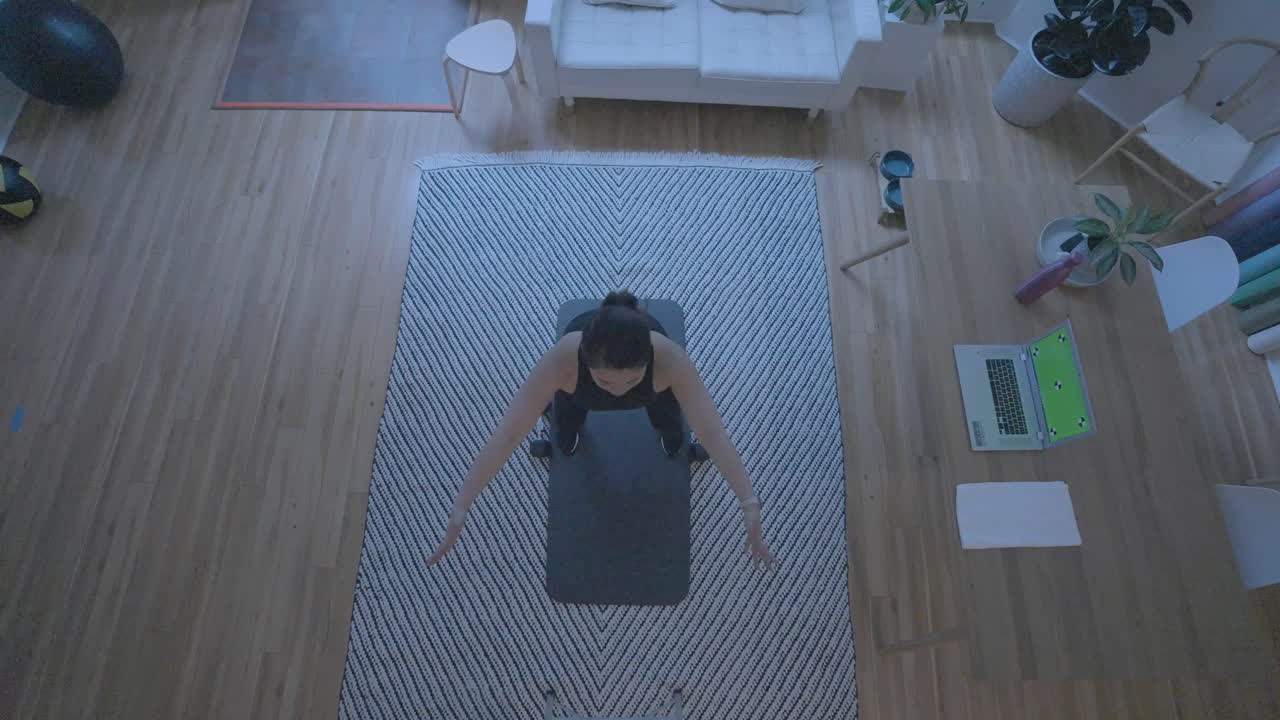 An overhead shot of a women doing stretches in front of a computer green screen at home in her living room