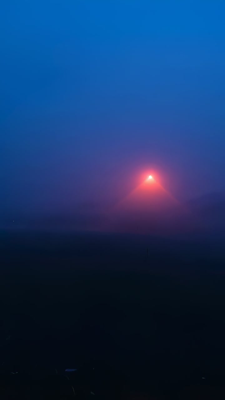 Vertical video: Pulsing red beacon casting triangular halo, fog scattering light over wide ground