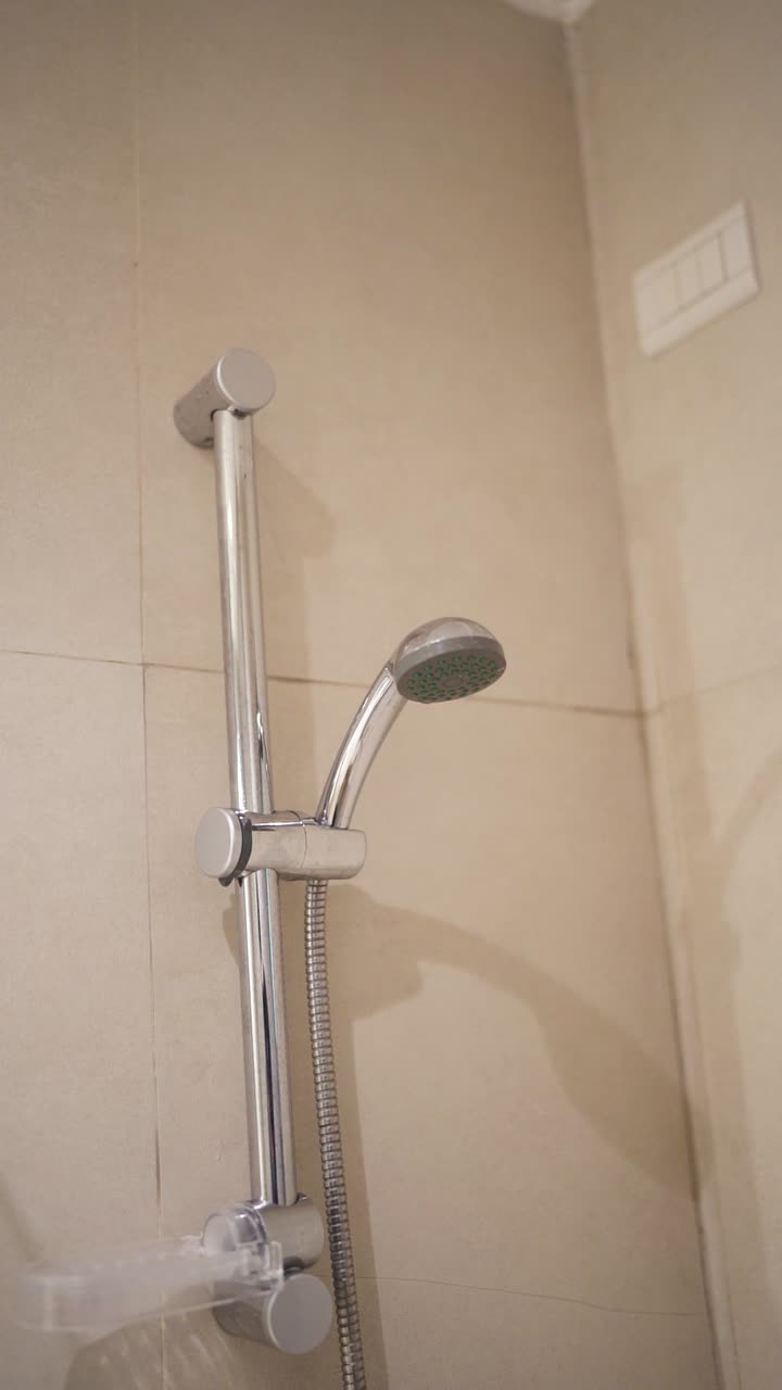 Close up camera shot inside bathroom shower at hotel, with light beige tiles and polished aluminum faucet.