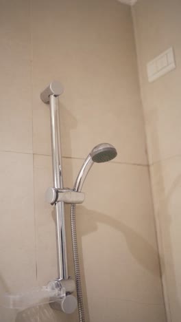 close up camera shot inside bathroom shower at hotel, with light beige tiles and polished aluminum faucet.