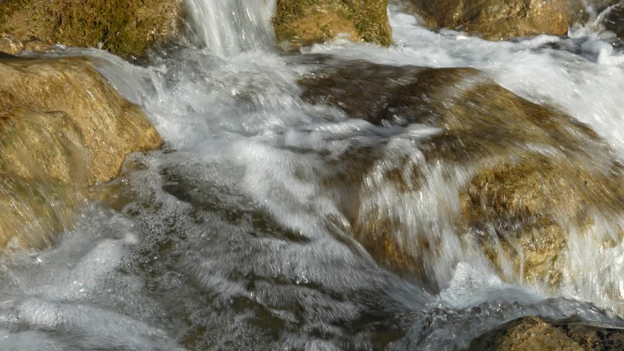 Primo piano di un ruscello di montagna cristallino che scorre veloce e si precipita su rocce muschiose in Svizzera.