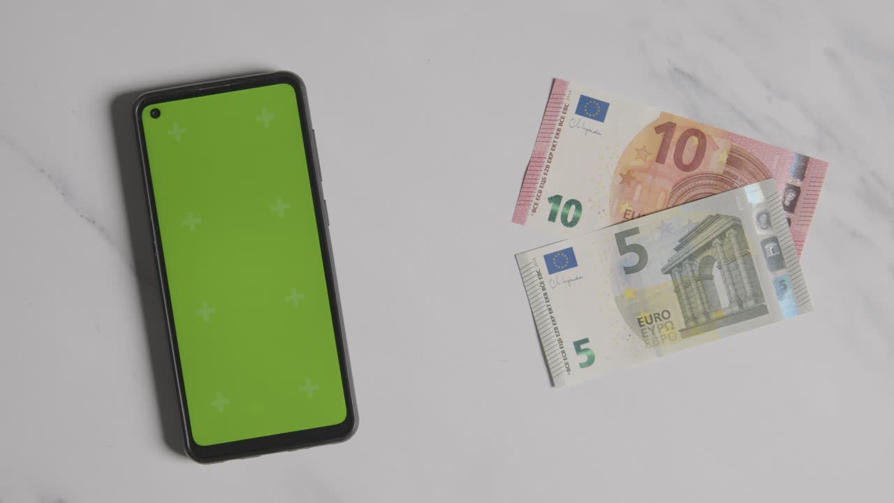 toma de moneda aérea de la mano agarrando billetes de 10 y 5 euros junto a un teléfono móvil de pantalla verde
