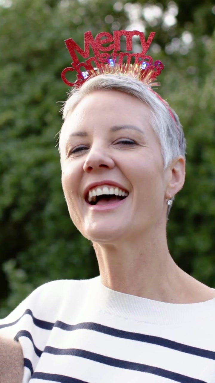Video verticale: Donna sorridente che ride mentre la telecamera si avvicina al giardino, con una fascia rossa glitterata.