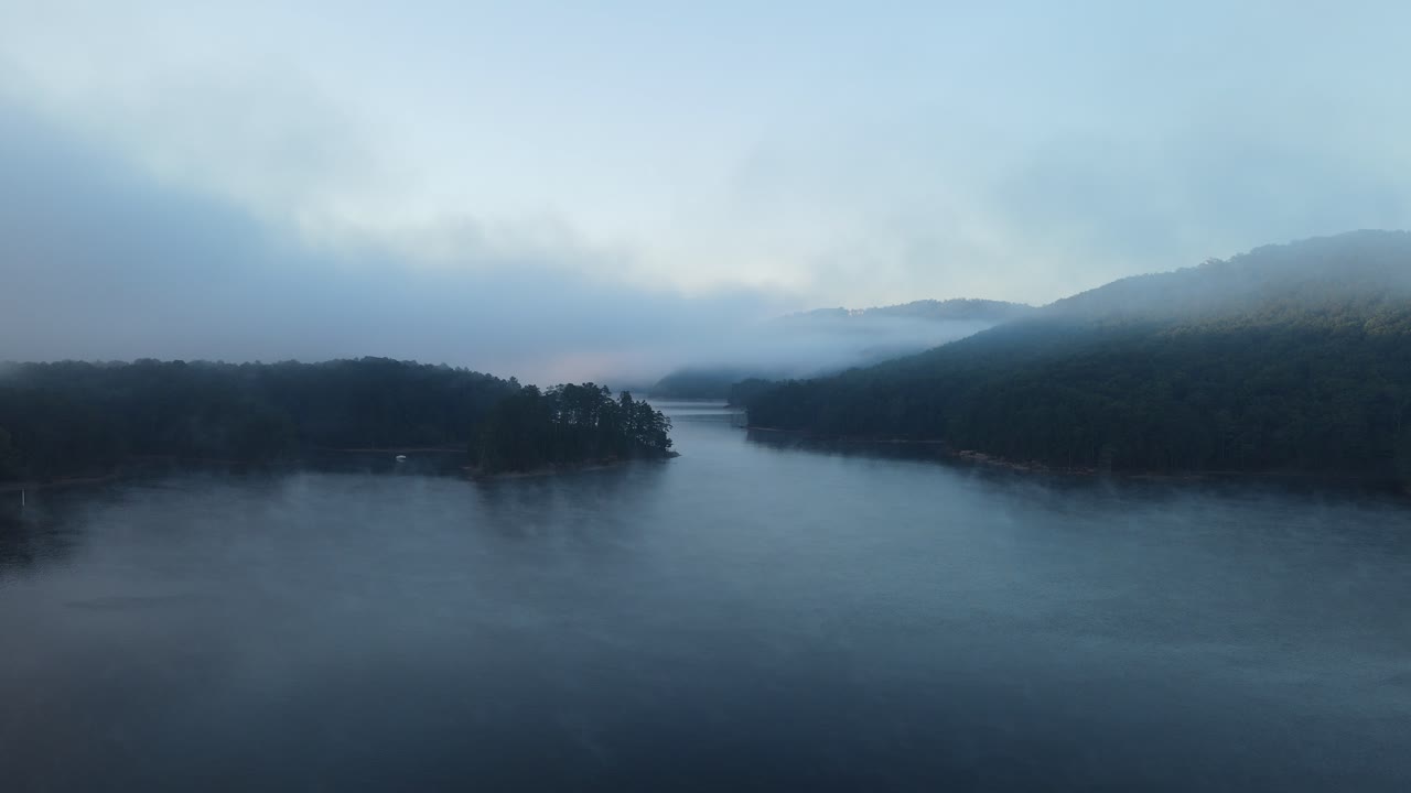 Flying over water towards mountains blanketed in fog clouds. Steam rising from the water creates an Erie blanket of fog. 4k 30fps