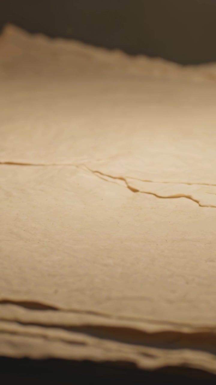Video verticale: La telecamera si sposta rivelando una pila di carta beige strappata su un tavolo illuminato da luce calda, mostrando la texture.